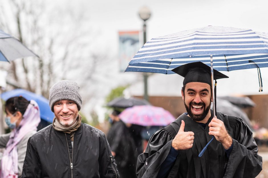 Happy Graduates holding an umbrella and giving a thumbs up