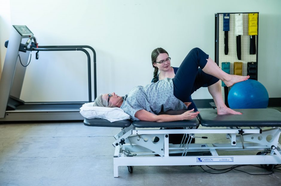 Client lying on a table next to a physical therapist receiving movement therapy in a clinic